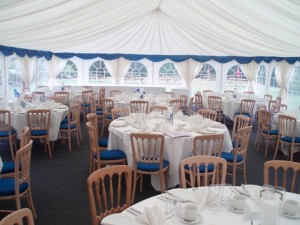 Marquee set up for a Wedding reception, with pleated ivory lining and blue valance and beachwood chairs with blue seat pads.